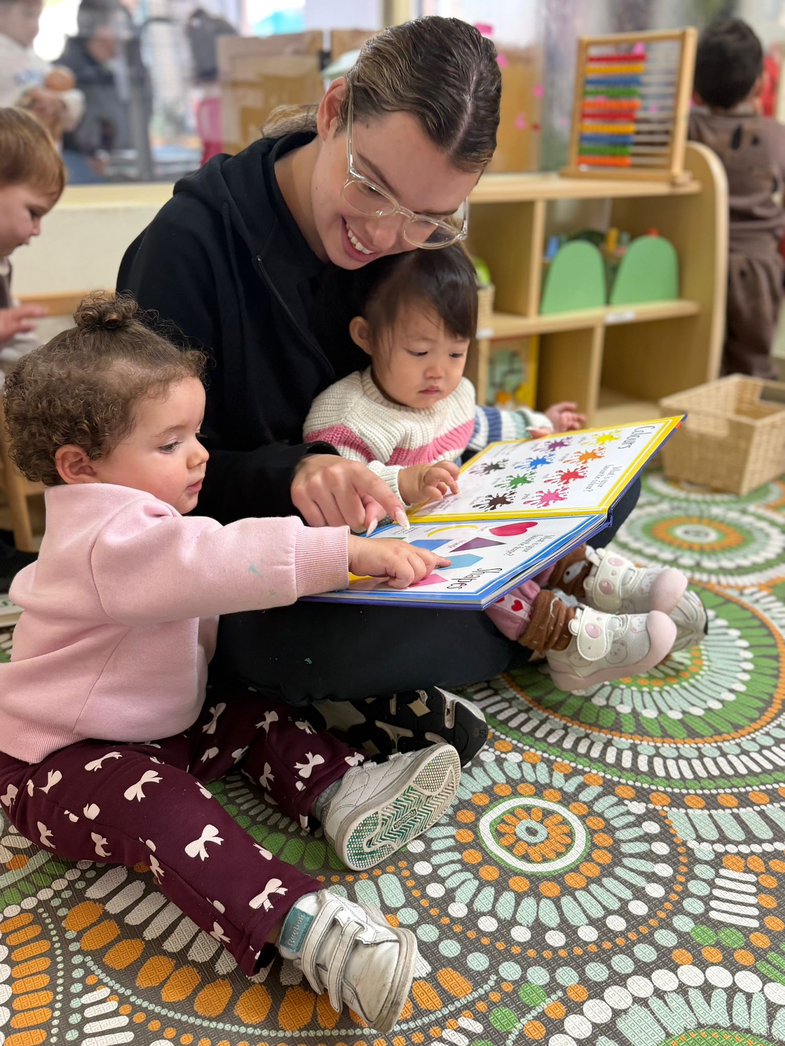 Cuddles 4 Kids Punchbowl early childhood educator reading an educational picture book to toddlers on a play mat