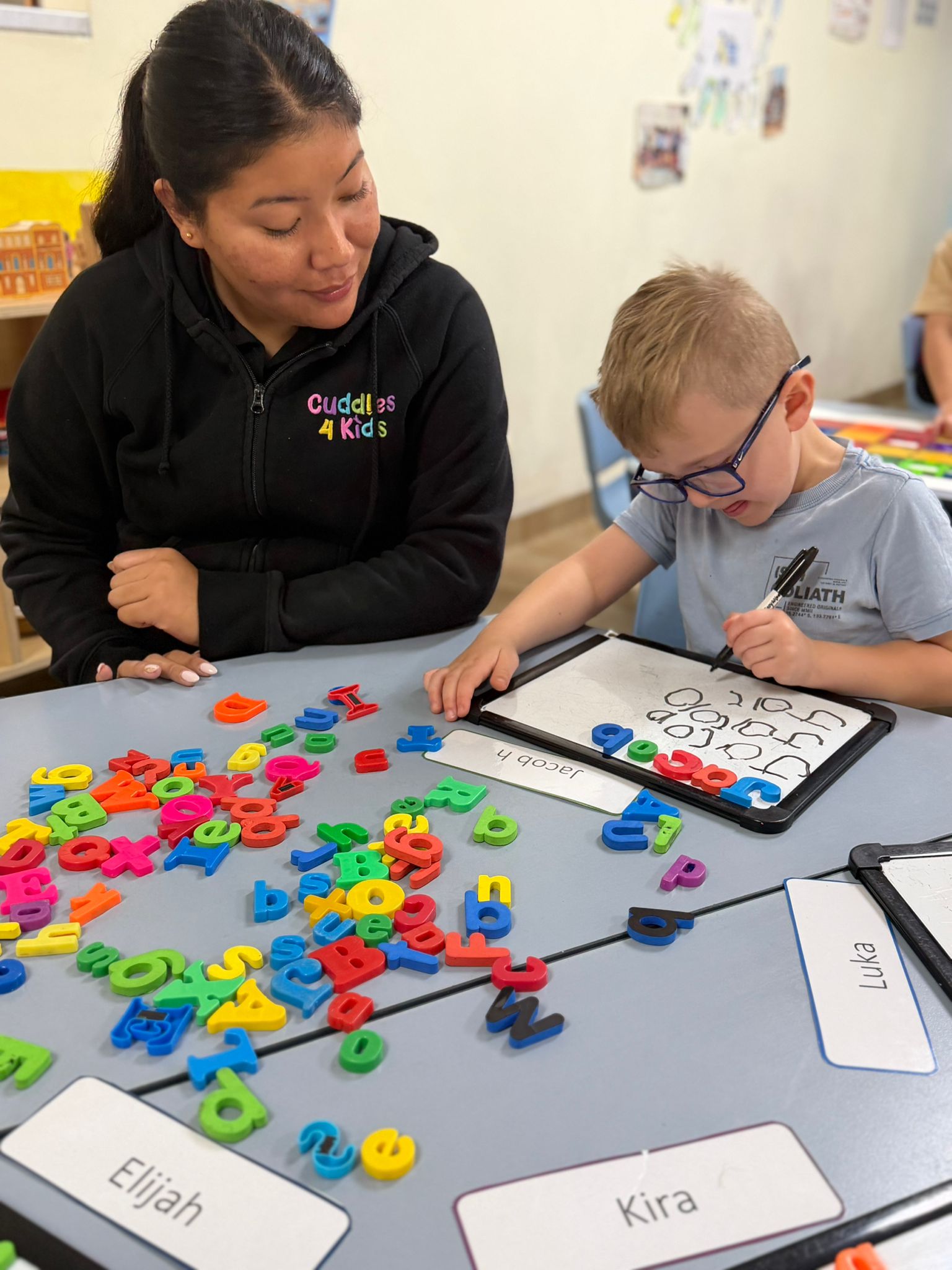 Cuddles 4 Kids Punchbowl educator helping a preschool child practice writing spelling letters on a whiteboard