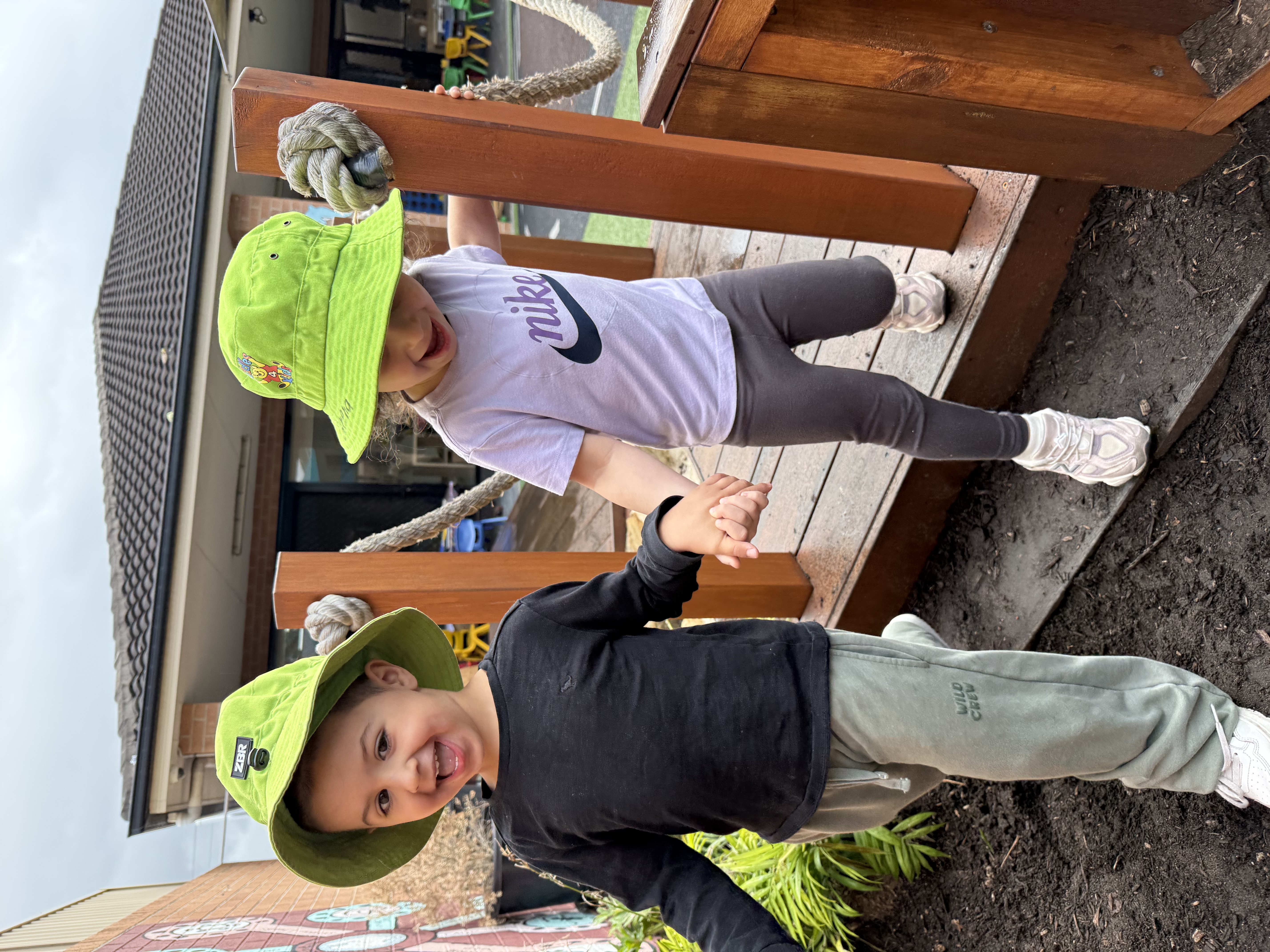 Two young children wearing green sun hats holding hands and playing outdoors