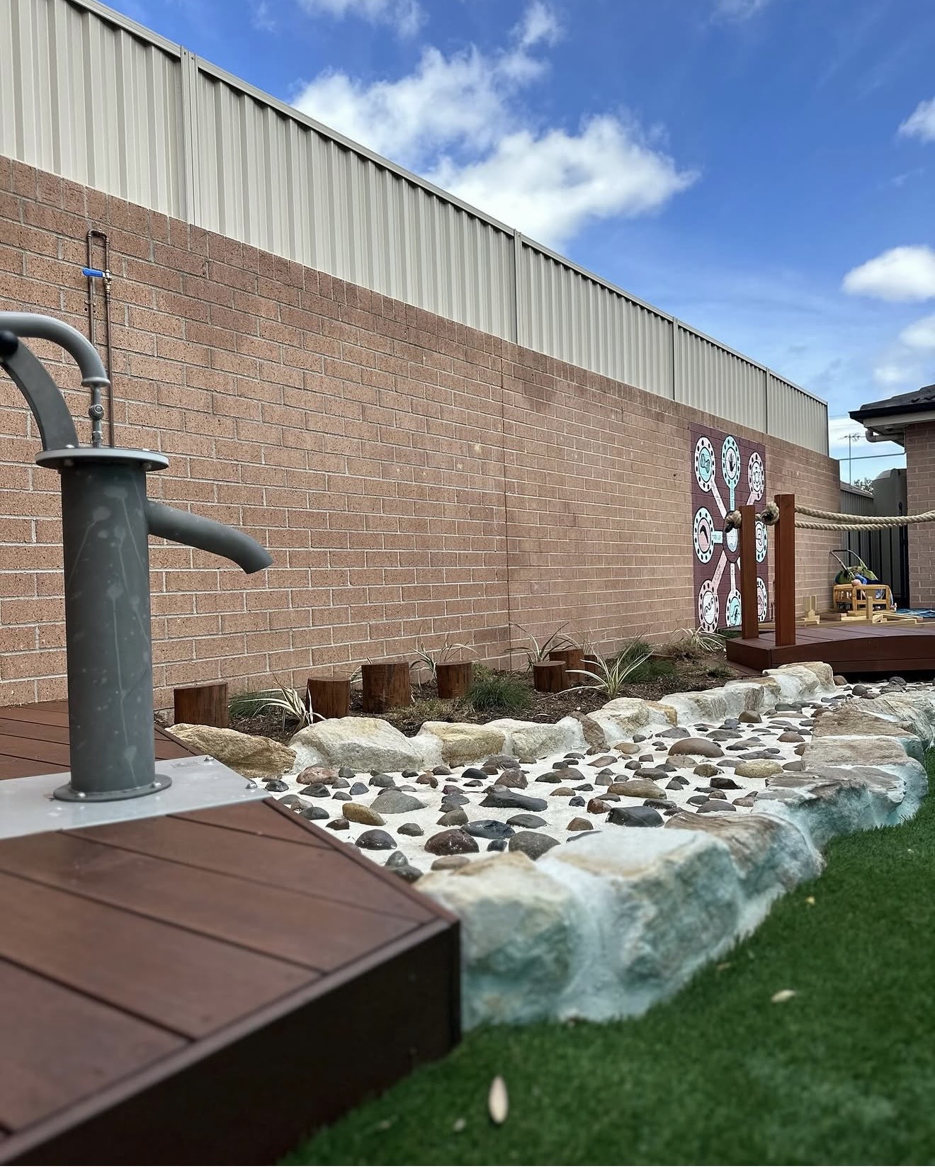 Secure outdoor play space showcasing an interactive rustic water pump feature and a landscaped rock garden